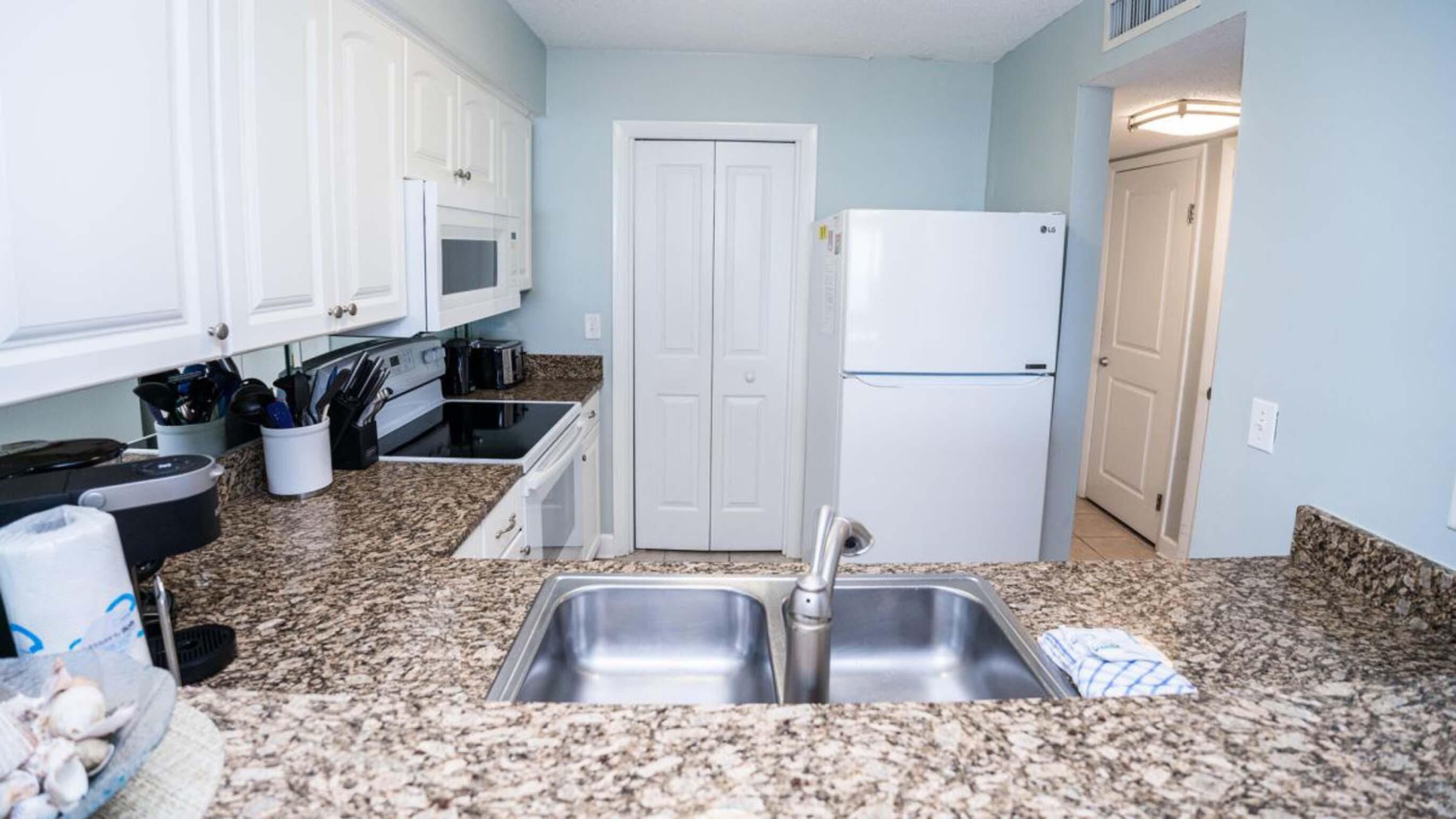 A kitchen with granite countertops, white cabinets, a double-door refrigerator, and a microwave.