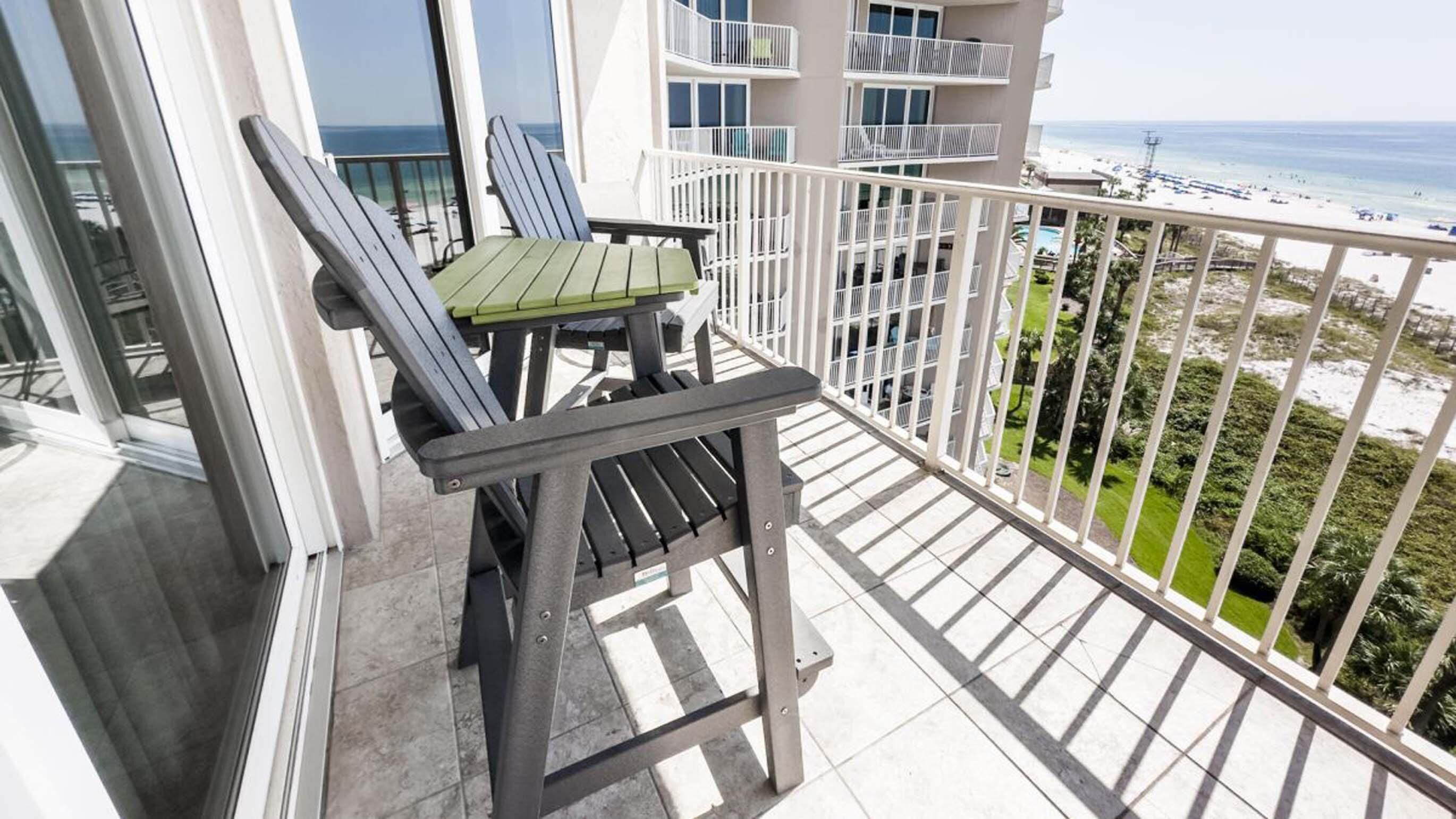 Un balcón con mesa y sillas, con vistas a una playa y un edificio con balcones.