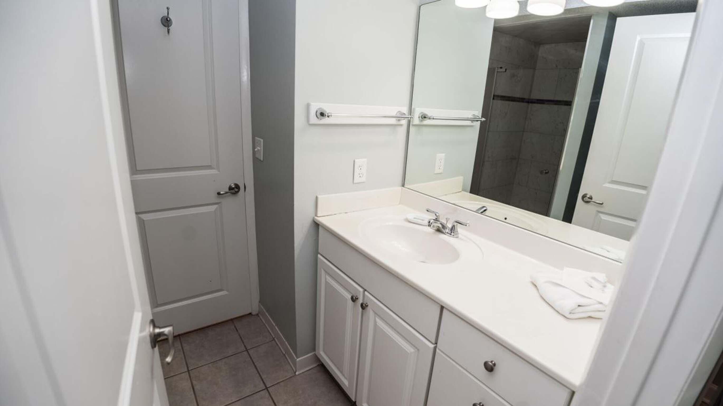 Un baño con lavamanos, espejo y puerta blancos.