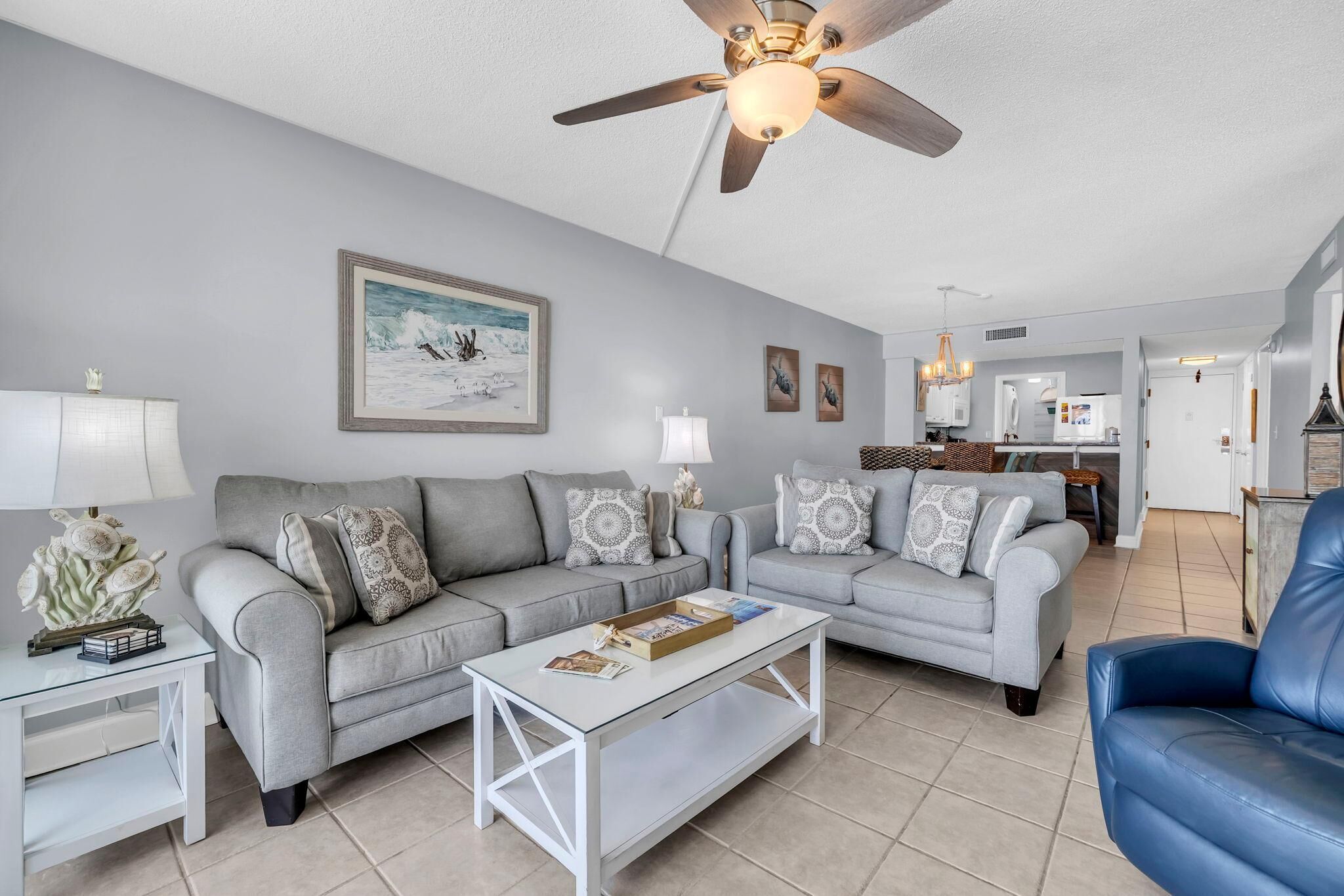 A living room with a grey sofa set, a coffee table, a blue armchair, and a ceiling fan.