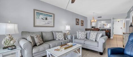 A living room with a grey sofa set, a coffee table, a blue armchair, and a ceiling fan.