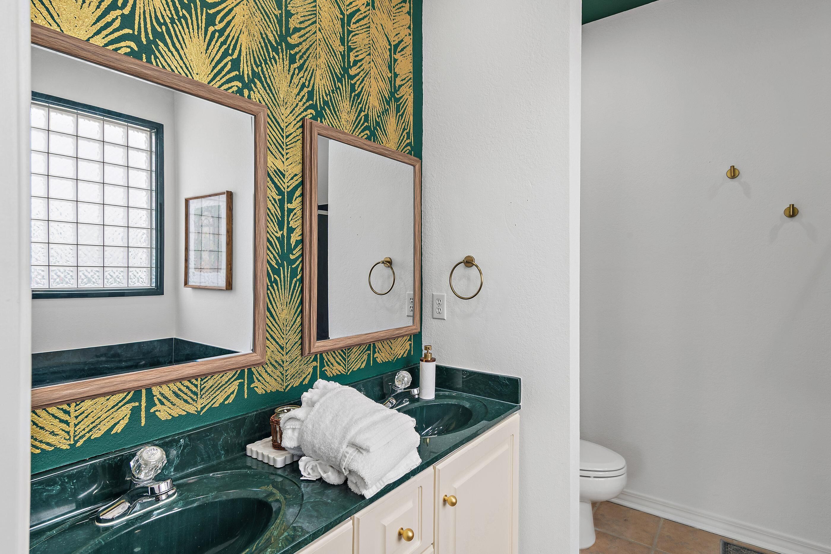 Une salle de bain avec un lavabo en marbre vert, un miroir, des toilettes et une fenêtre à motifs géométriques.