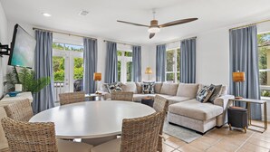 Un salon moderne avec une table de salle à manger ronde, des chaises en osier, un canapé et un ventilateur de plafond.