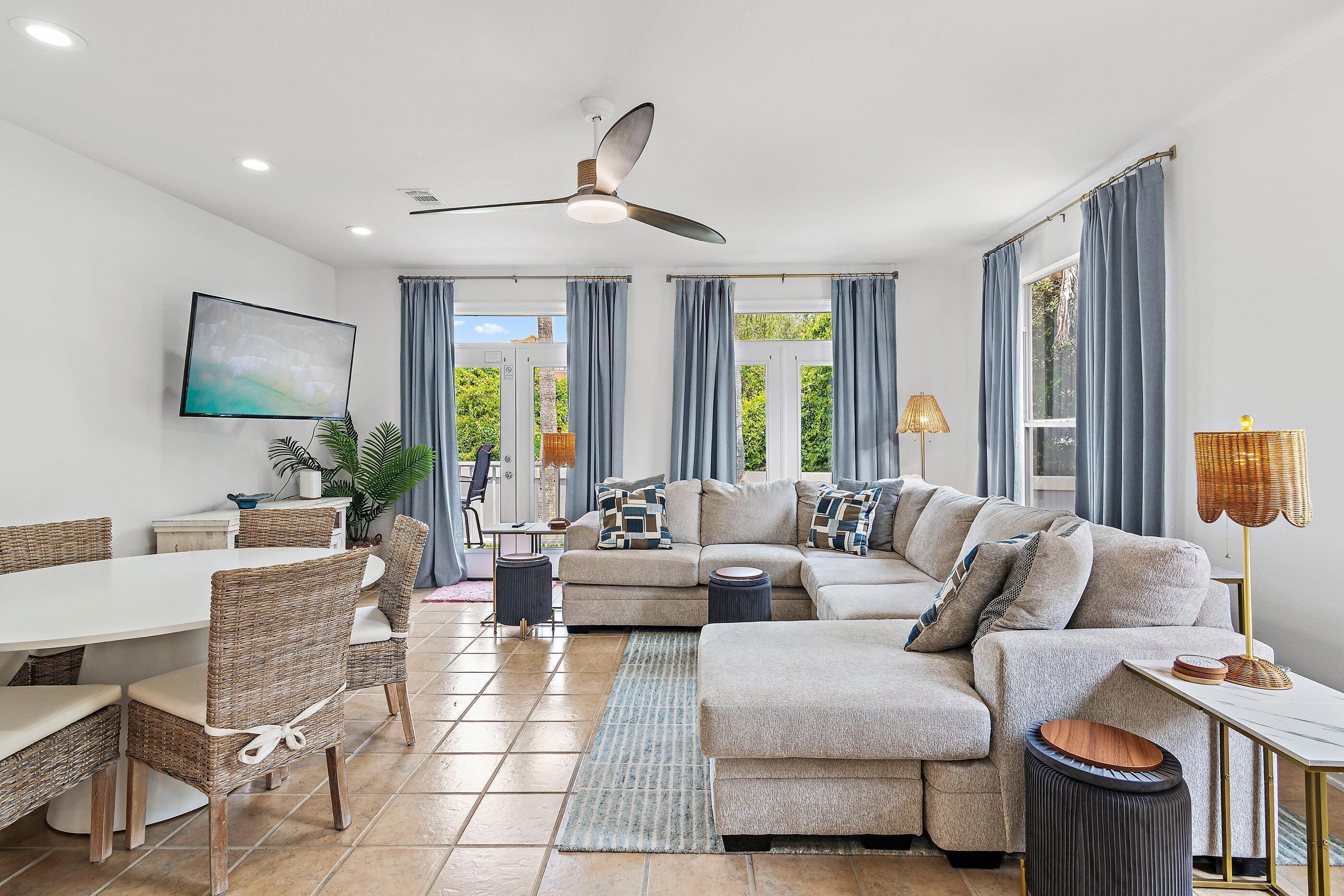 A modern living room with a sectional sofa, dining table, chairs, and a ceiling fan.
