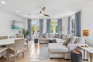 A modern living room with a sectional sofa, dining table, chairs, and a ceiling fan. - Peachy Palm (Destin)