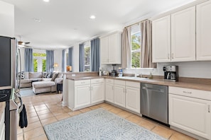 A modern kitchen with white cabinets, a stainless steel dishwasher, and a coffee maker. - Peachy Palm (Destin)