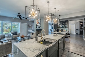 A modern kitchen with a central island, pendant lights, and a dining area with a sofa and chairs. - Massage Chairs, Foosball, Wet Bar & Board Games (Roanoke)