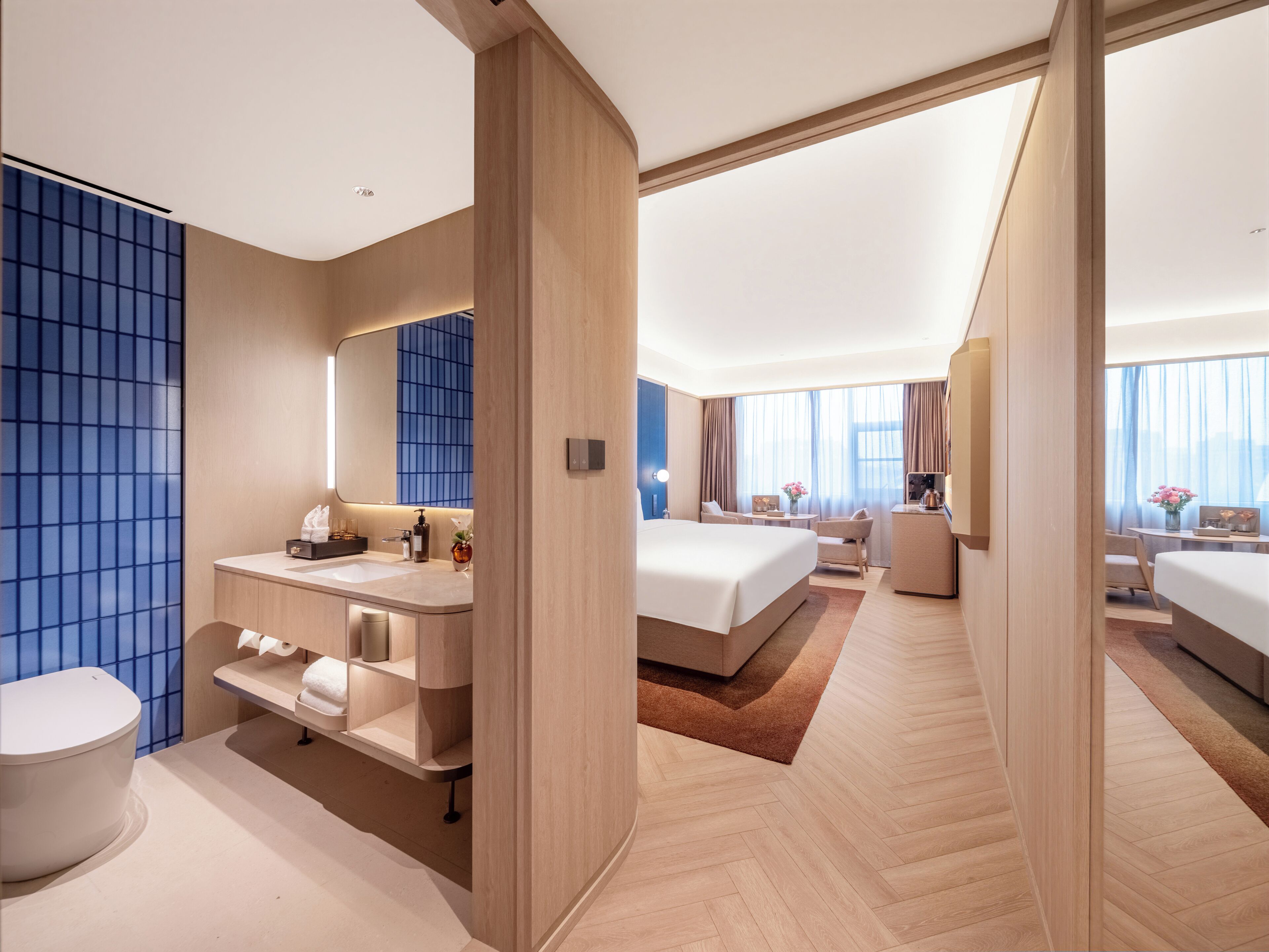 A modern hotel room with a large bed, a separate bathroom, a desk, and a seating area.