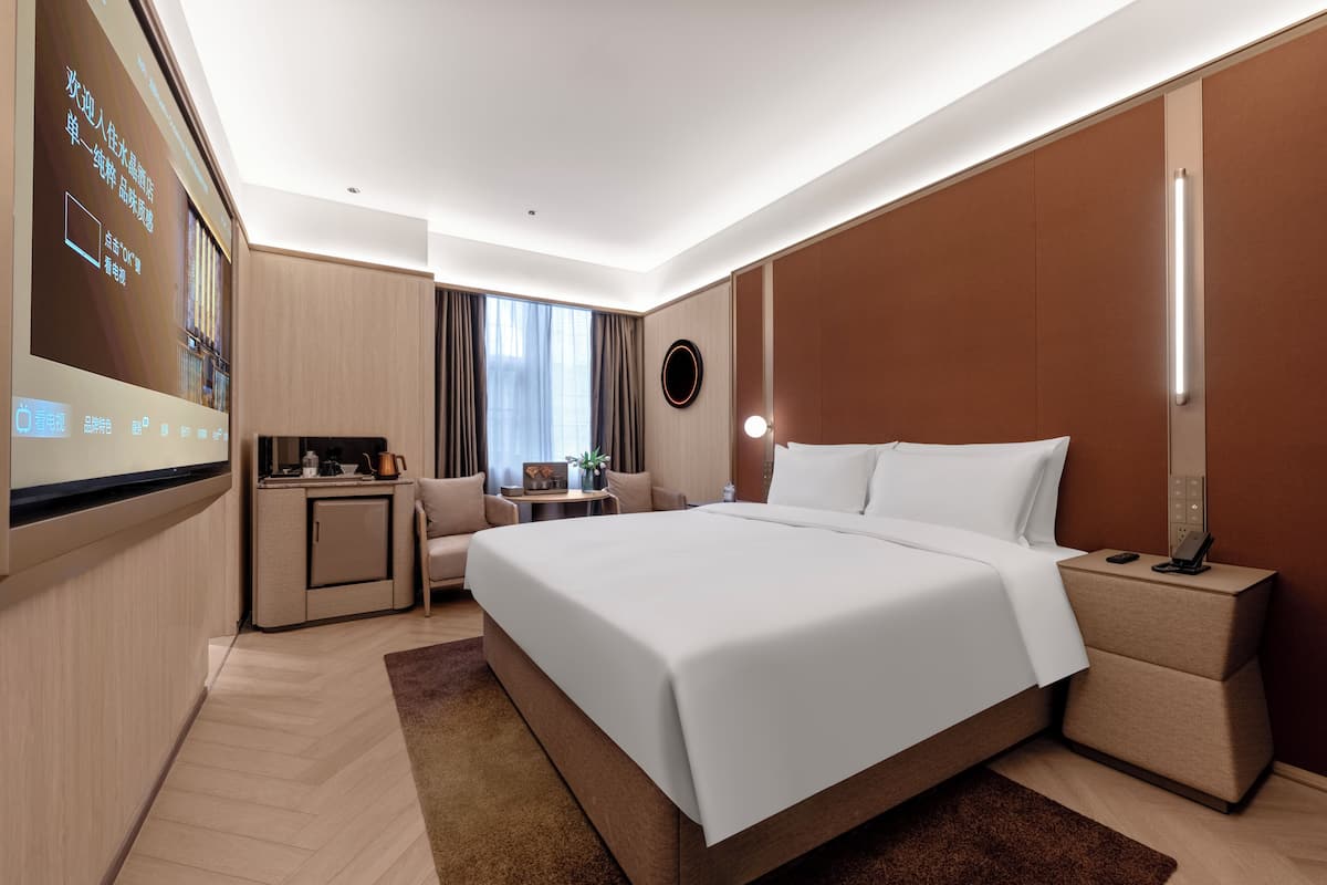 A modern hotel room with a large bed, bedside tables, a desk, and a television screen displaying information.