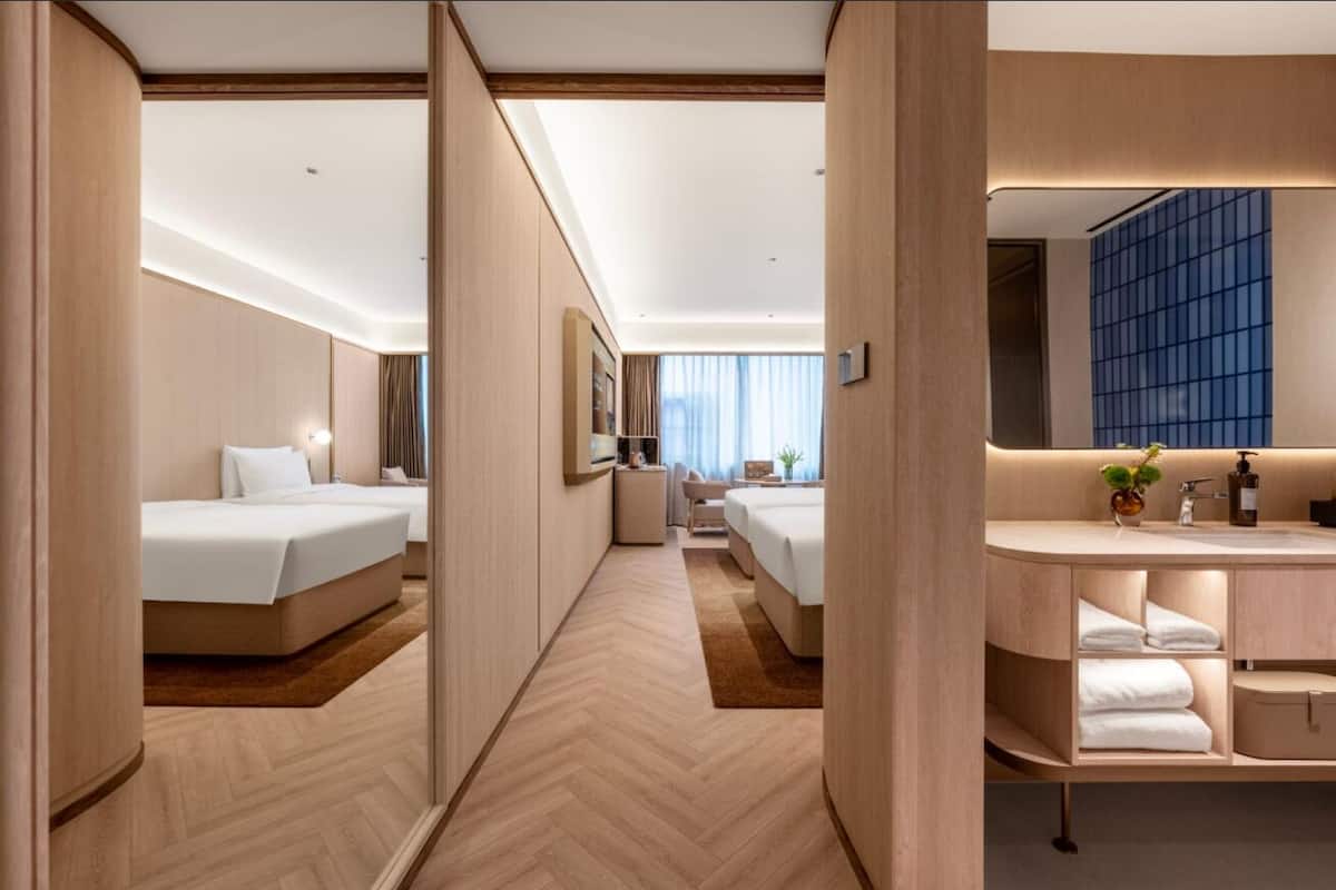 A hotel room with two beds, a bathroom with a large mirror, and a view of the city.