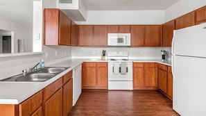 A modern kitchen with wooden cabinets, a stainless steel sink, a microwave, an oven, and a refrigerator.