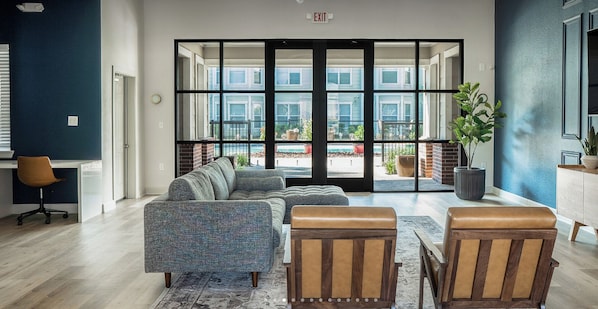 Ein modernes Interieur mit einer Eckcouch, zwei Ledersesseln, einem Blumentopf und Blick durch große Glastüren auf einen Außenbereich.