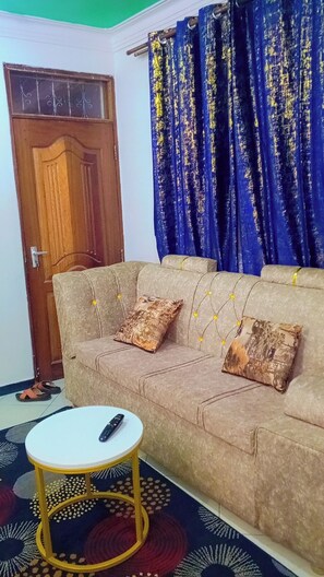 A living room with a sofa, two cushions, a round coffee table, a remote control, and a patterned rug. - Welcoming 1-bedroom apartment in vibrant Mombasa perfect for relaxing (Mombasa)