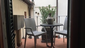 Een balkon met een tafel, twee rieten stoelen, een bloempot en een decoratieve vaas.