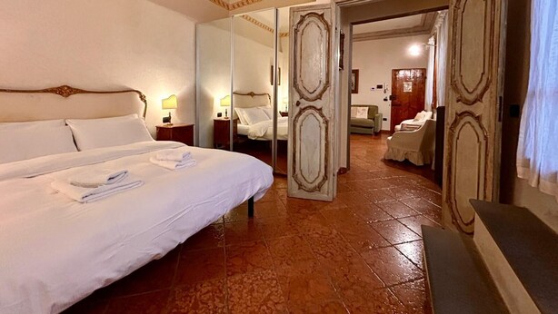 Een hotelkamer met een groot bed, een spiegel, een kledingkast en een deur naar een andere kamer.
