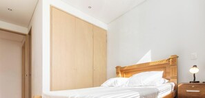 A bedroom with a wooden wardrobe, a bed with white bedding, and a nightstand with a lamp. - Luxury 3 Bedroom Apartment in Provence (Medellín)
