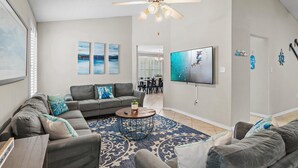 A living room with a ceiling fan, grey sofas, a coffee table, and a TV mounted on the wall. - Bamba's Beach House (Destin)