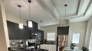 A modern kitchen with dark cabinetry, a central island, and pendant lighting. - Beautiful Apartment with 4 Beds in Gated Community Close of Shops (McAllen)