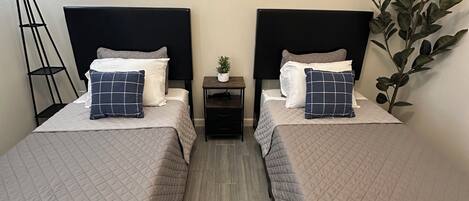 Een hotelkamer met twee bedden, een kleine tafel, een vloerlamp en drie ingelijste foto’s aan de muur.