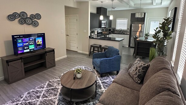 A modern living room with a sectional sofa, a coffee table, a TV, and a ceiling fan. - Beautiful Apartment with 4 Beds in Gated Community Close of Shops (McAllen)