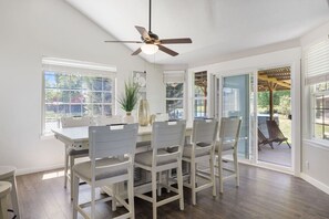 Un espace repas comprenant une table et des chaises, un ventilateur de plafond et de grandes fenêtres.