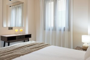 Habitació d'hotel amb un llit, una taula de nit amb una làmpada, un mirall i cortines translúcides.