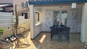 A patio with two tables and chairs, a small plant, and a white fence.