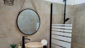 A bathroom with a round mirror, a vessel sink, a handheld showerhead, and wicker baskets.