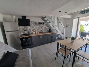 Une cuisine moderne dotée d’un four encastré, un coin repas avec une table et des chaises en bois, et un escalier menant à un autre niveau.