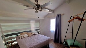 A bedroom with a bed, a ceiling fan, a window with curtains, a wooden floor, and a hanging chair.
