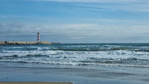 A lighthouse by the sea with waves crashing onto the shore.