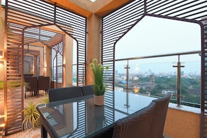 A balcony with a glass table, wicker chairs, and a potted plant.