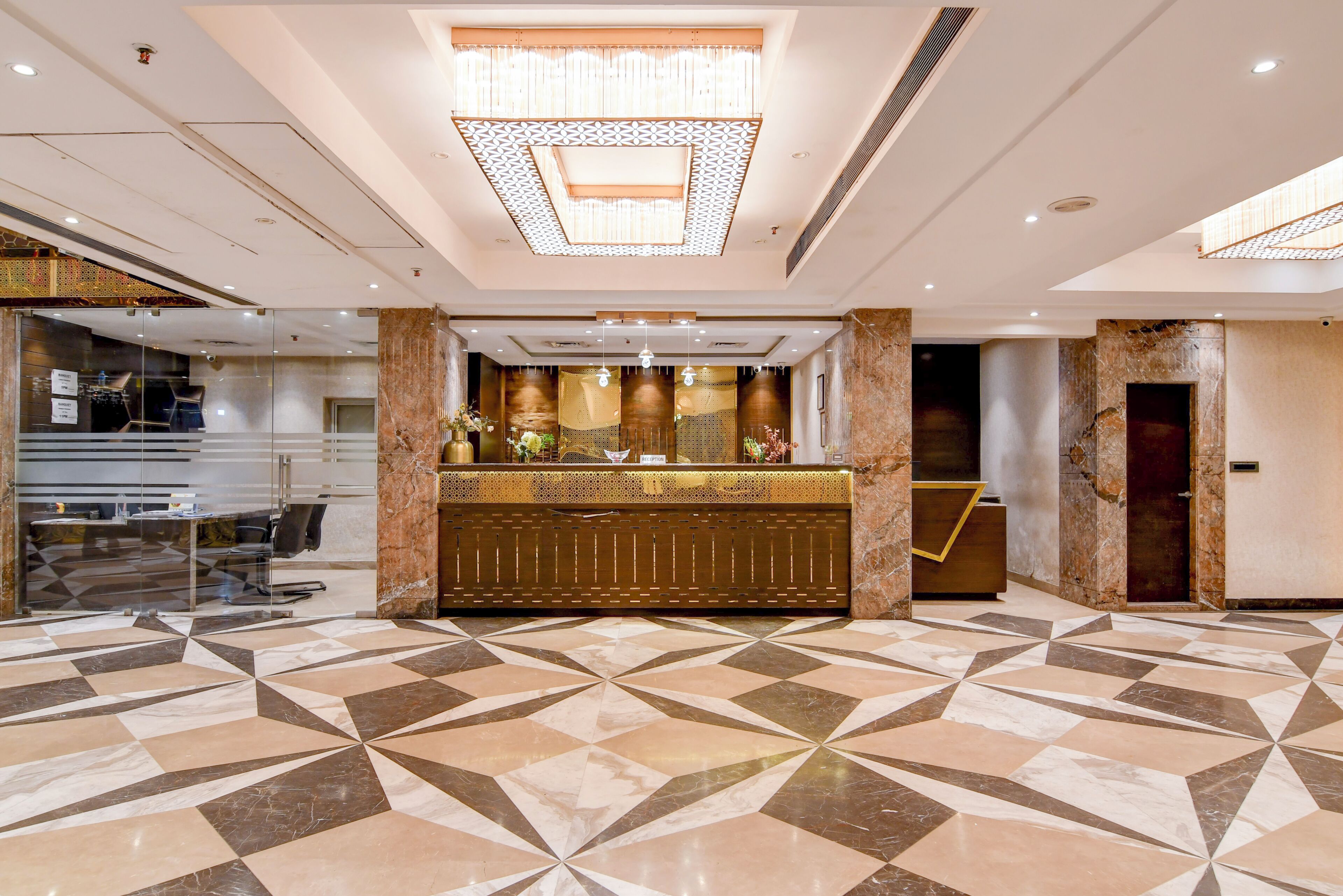 A hotel lobby with a geometric patterned floor, a reception desk, and a modern chandelier.