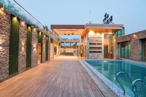 A poolside area with a wooden deck, stone walls, and a glass-enclosed pool.