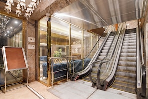 An indoor escalator, glass doors, a sign, and a blue sofa.
