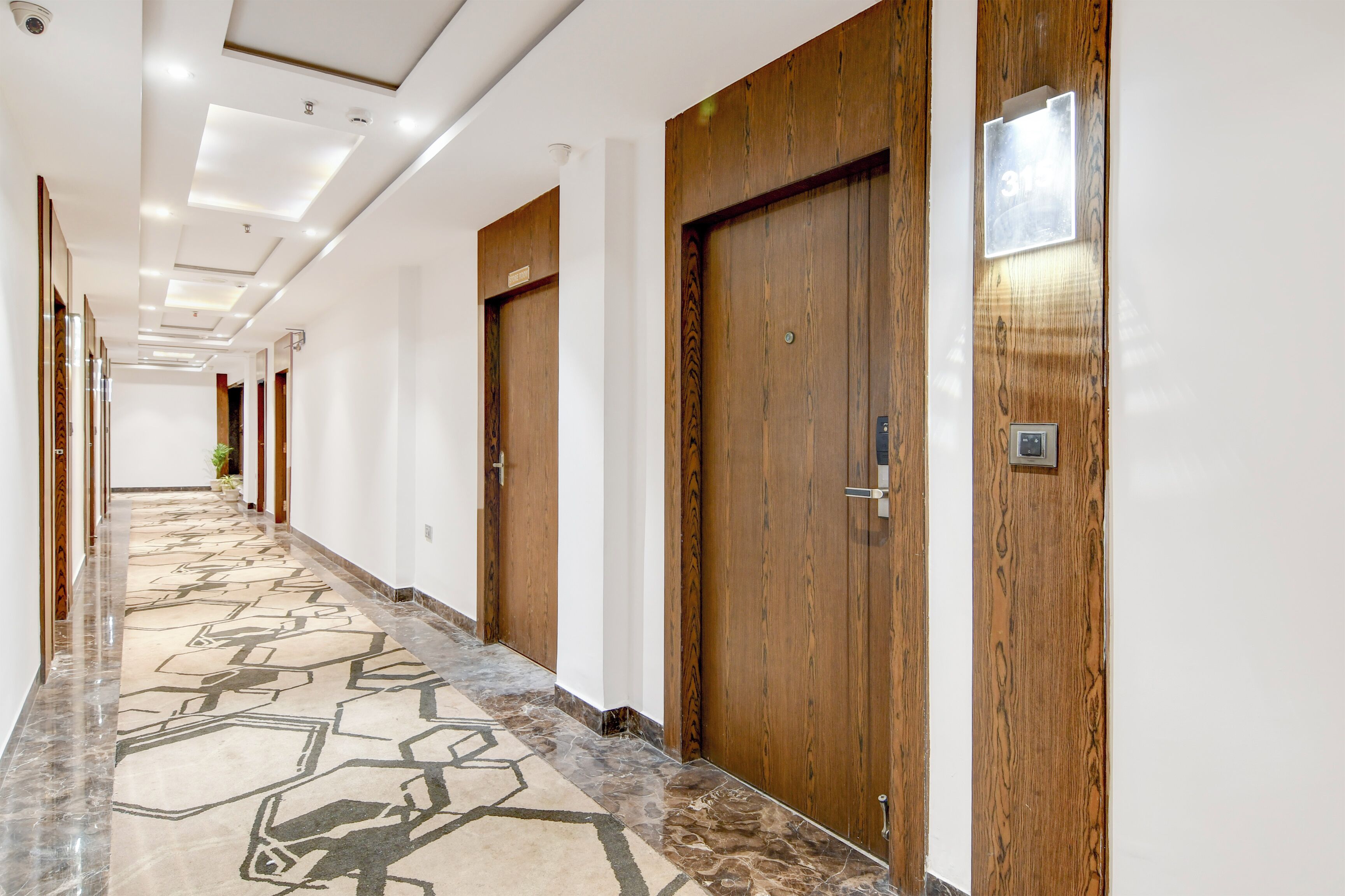 Un pasillo de hotel con puertas de madera, suelo de mármol e iluminación empotrada en el techo.