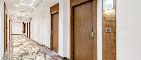 Un pasillo de hotel con puertas de madera, suelo de mármol e iluminación empotrada en el techo.