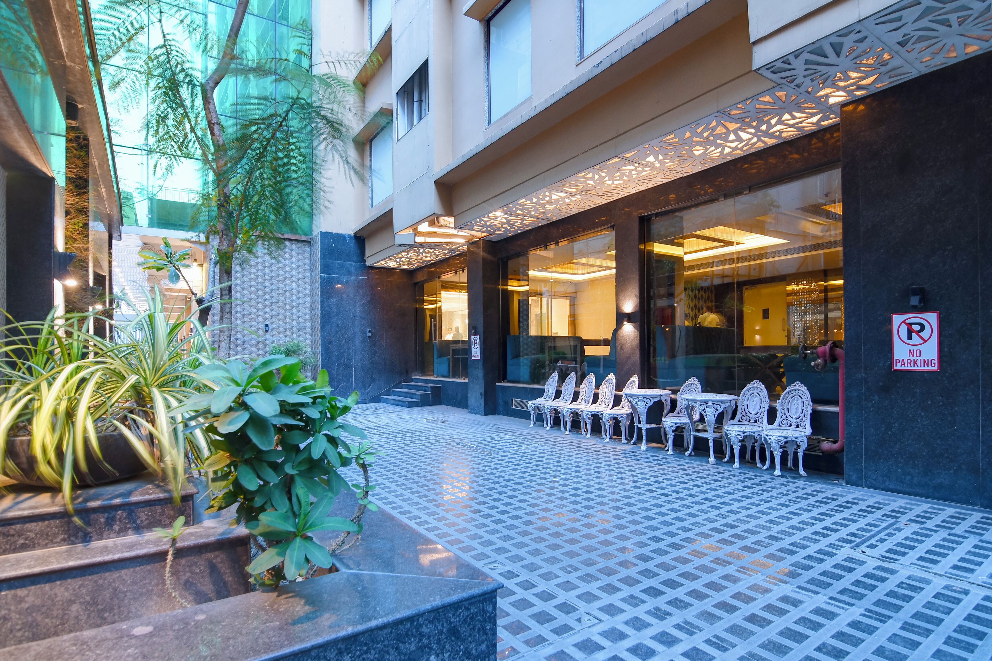 An outdoor seating area with tables and chairs, a 'No Parking' sign, and a building entrance with glass doors.