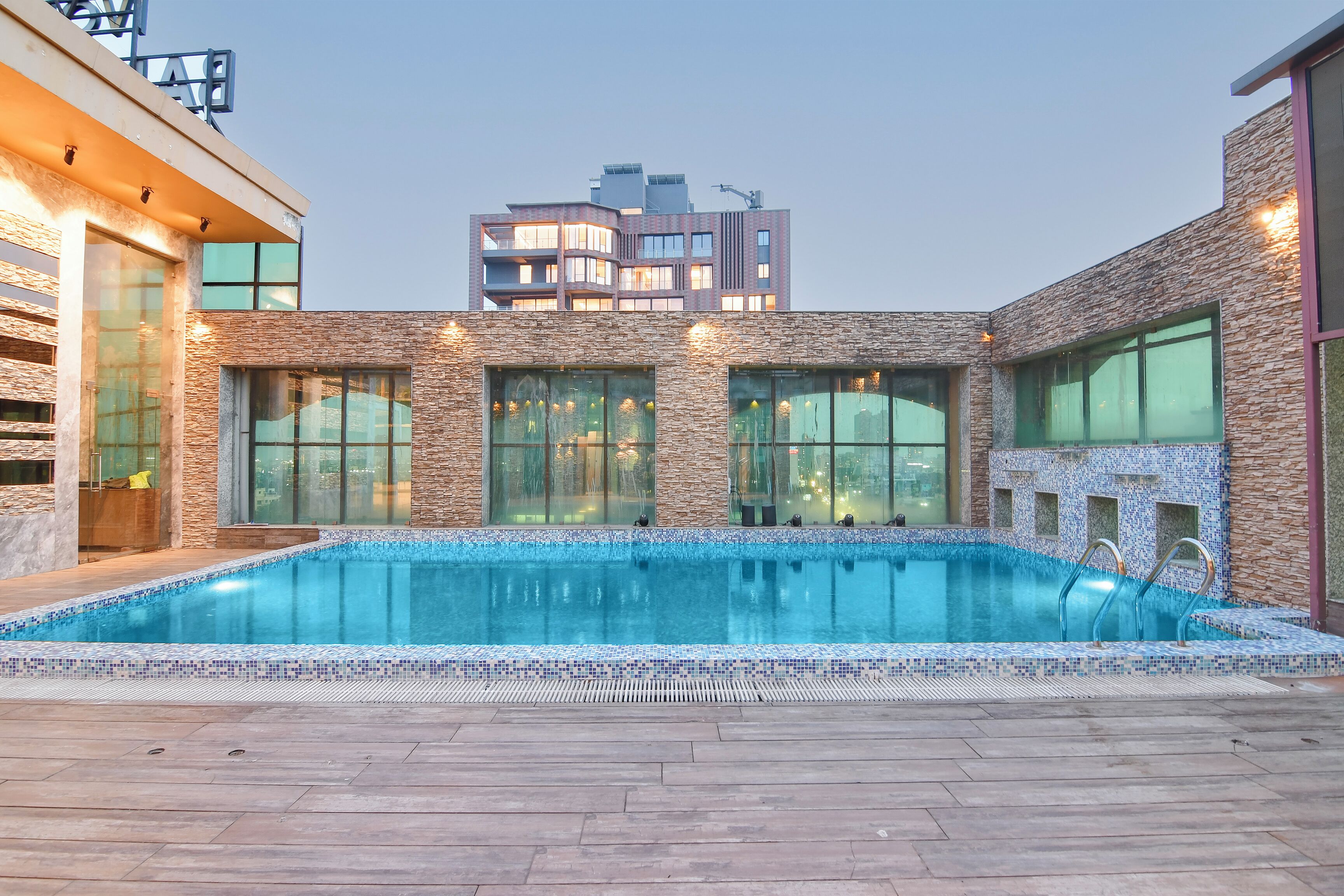 Una piscina con borde de azulejos, ventanas amplias y vista a un edificio moderno al fondo.