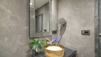 A bathroom with a marble wall, a gold sink, a mirror, and a potted plant.
