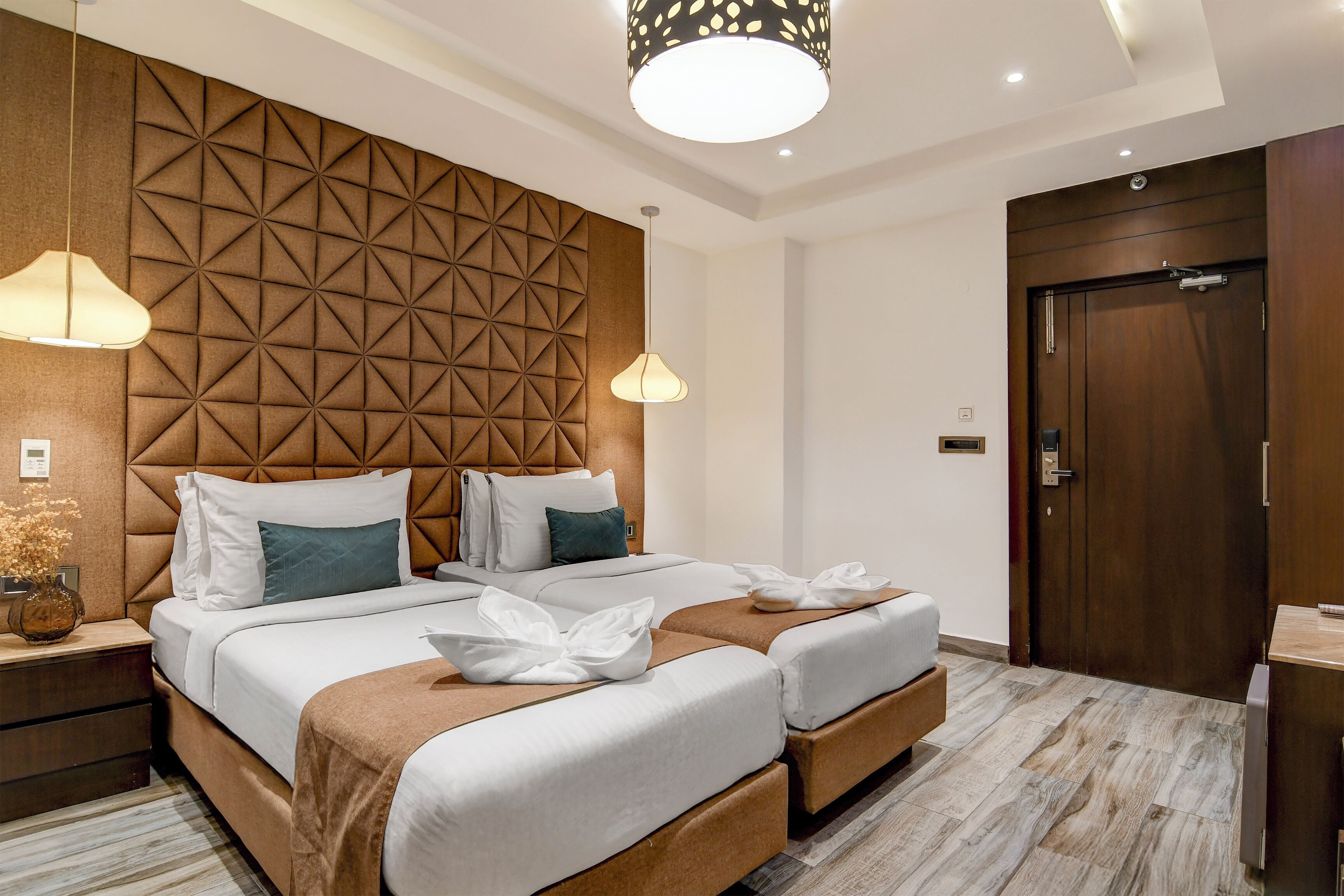 Ein Hotelzimmer mit modernem Design, mit einem großen Bett, dessen Kopfteil ein geometrisches Muster aufweist, zwei Nachttischen, einem Holzschrank und einem großen Spiegel.
