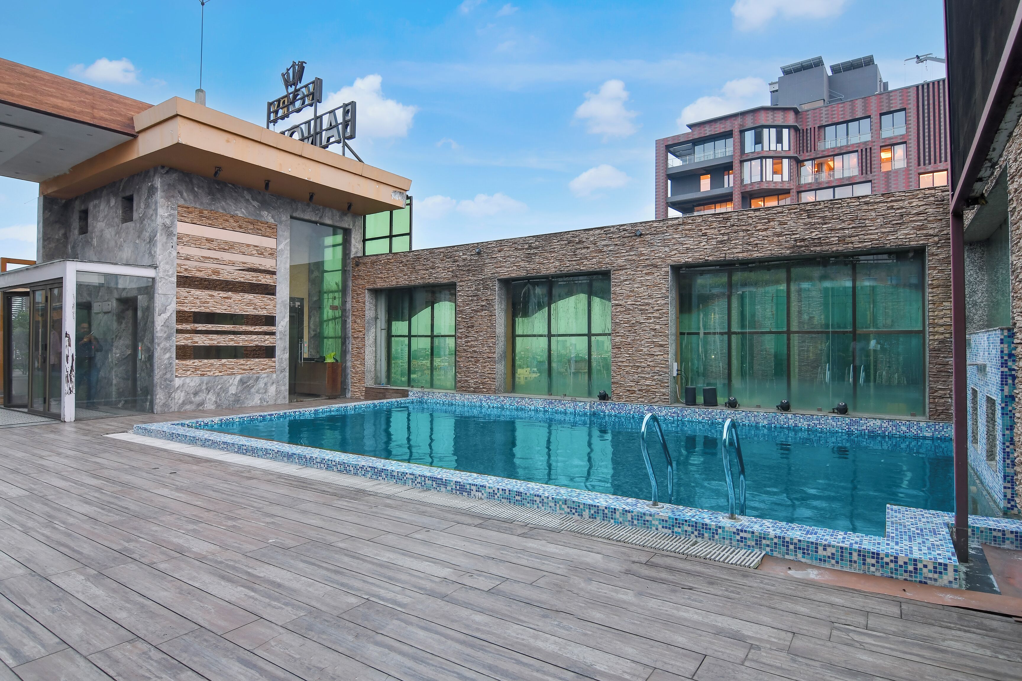 A swimming pool with a tiled edge, a wooden deck, and a building with large windows and a stone facade.