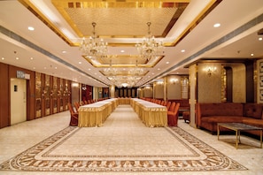 A long conference table with chairs, a sofa, and a patterned carpet in a well-lit room with chandeliers.