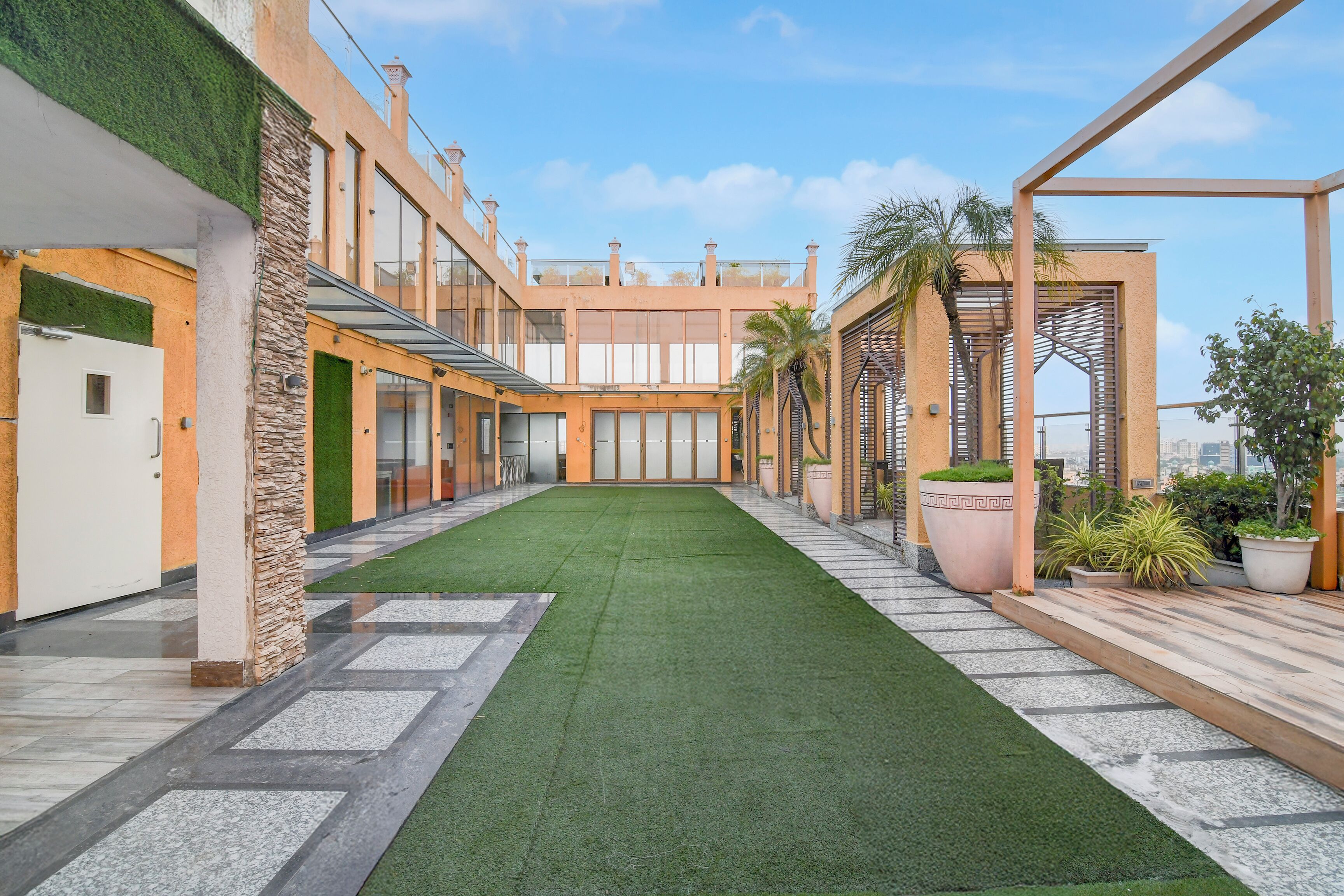 A courtyard with artificial grass, a pool, and a pergola with plants.