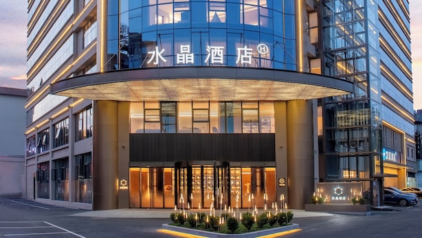 Een modern hotel met een gebogen entree, verlichte signage en een parkeerplaats.