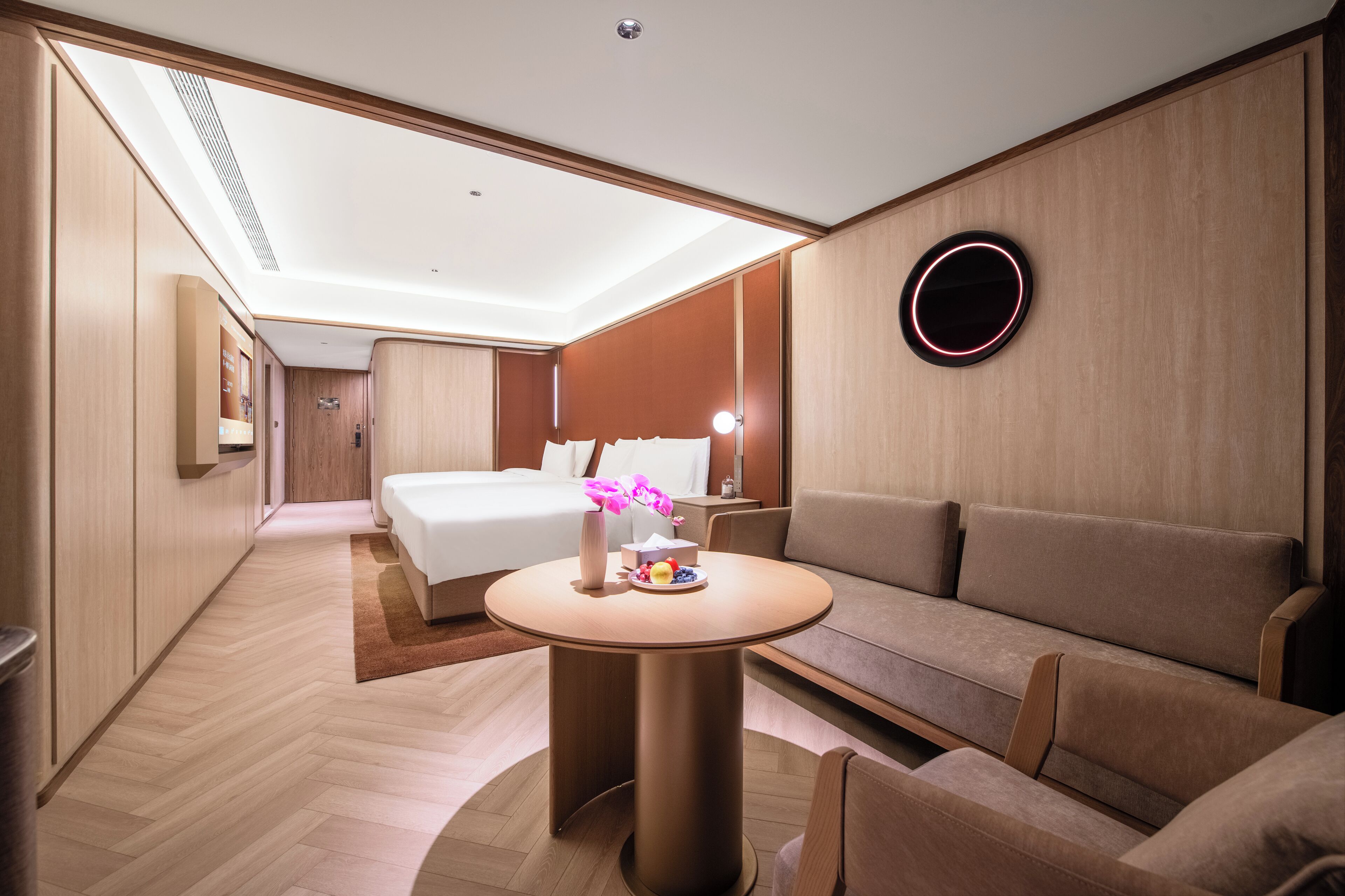 A modern hotel room with a bed, sofa, round table, and a wall-mounted circular light fixture.