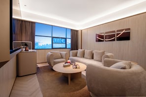 A modern hotel room with a large window, a sofa, a coffee table, and a small desk.