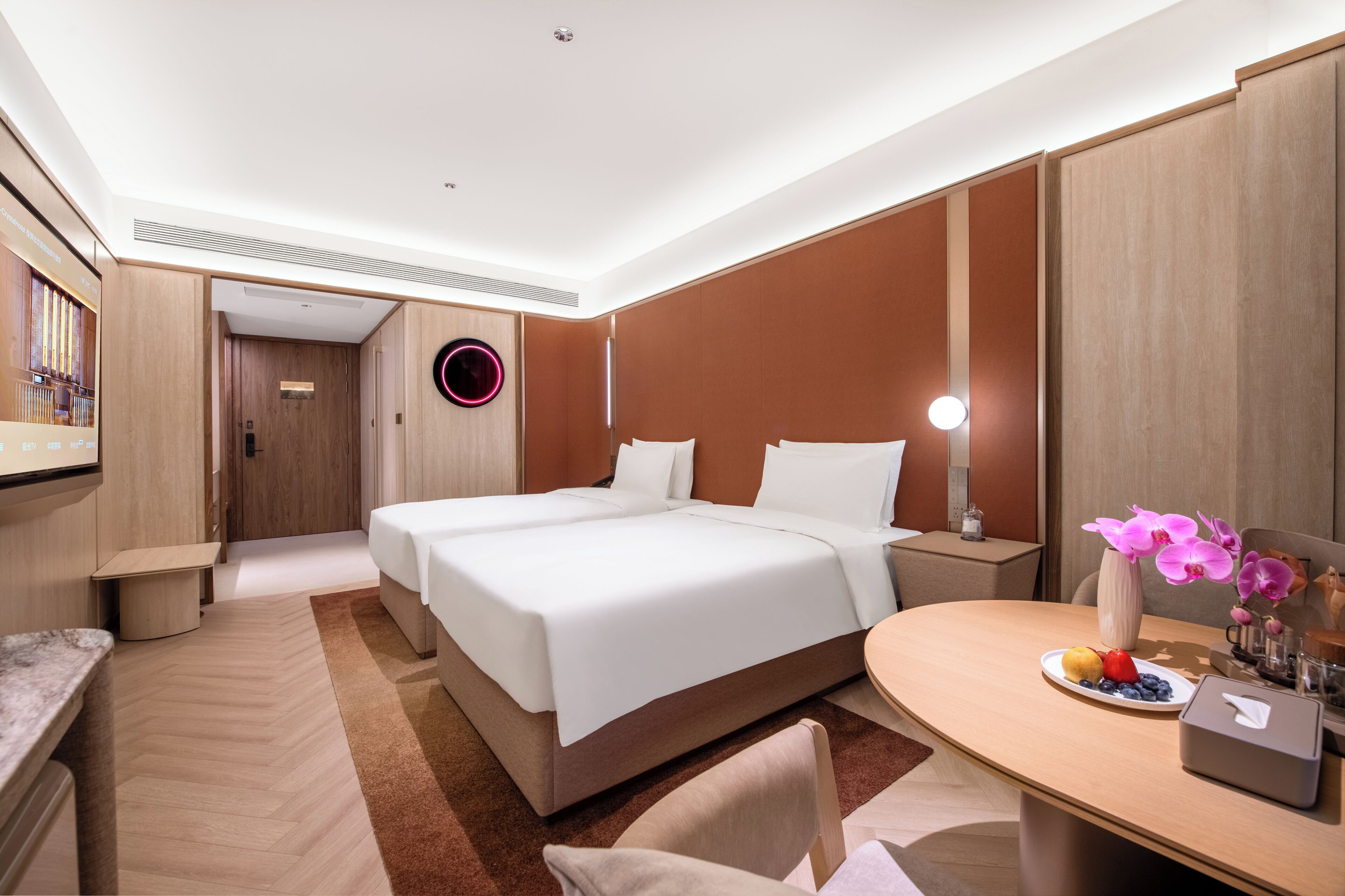 A hotel room with a large bed, bedside tables, a desk, a chair, and a round mirror.