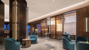 Een moderne lobby met zithoeken, een hoge decoratieve kolom en een groot raam met gordijnen.