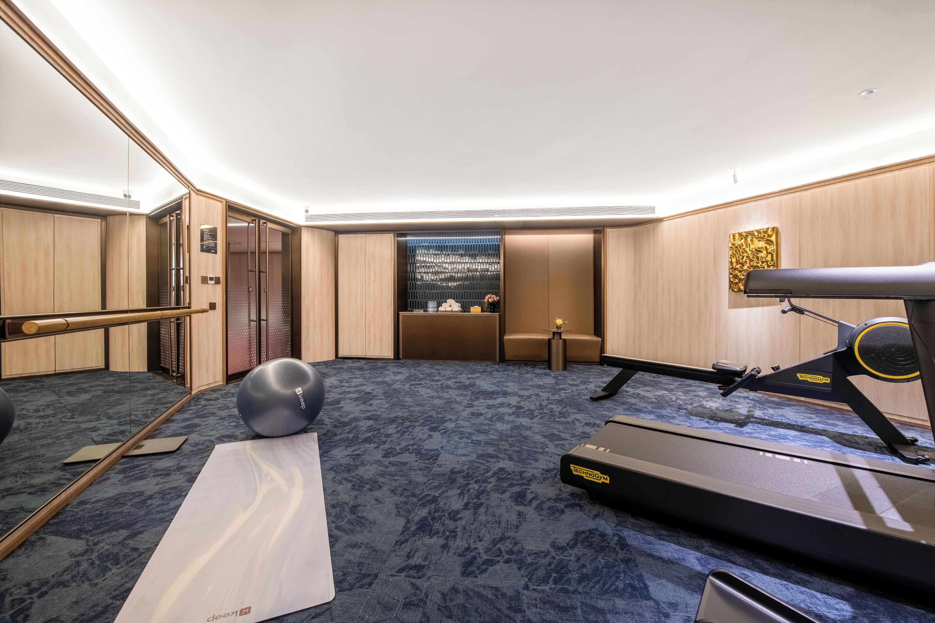 A hotel room with a treadmill, exercise ball, and a mirror.